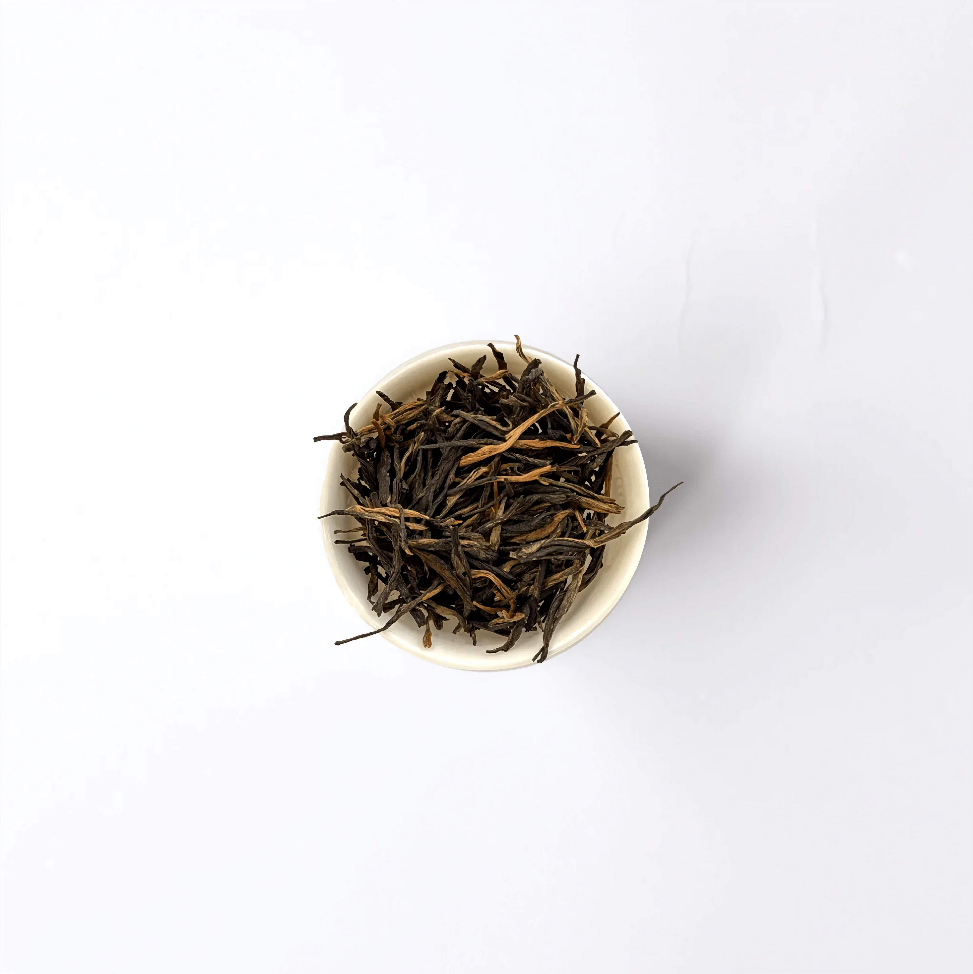 Czerwona herbata Dian Hong Jin Zhen - złociste pąki w białej miseczce na drewnianym stole